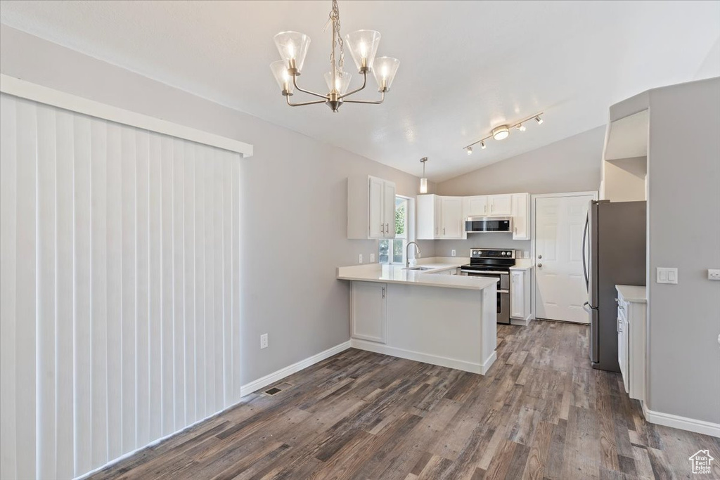 Kitchen featuring appliances with stainless steel finishes, a peninsula, dark wood-style floors, lofted ceiling, and light countertops
