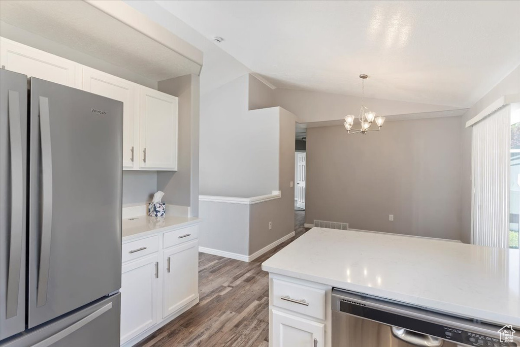 Kitchen featuring stainless steel appliances, lofted ceiling, white cabinetry, wood finished floors, and a chandelier