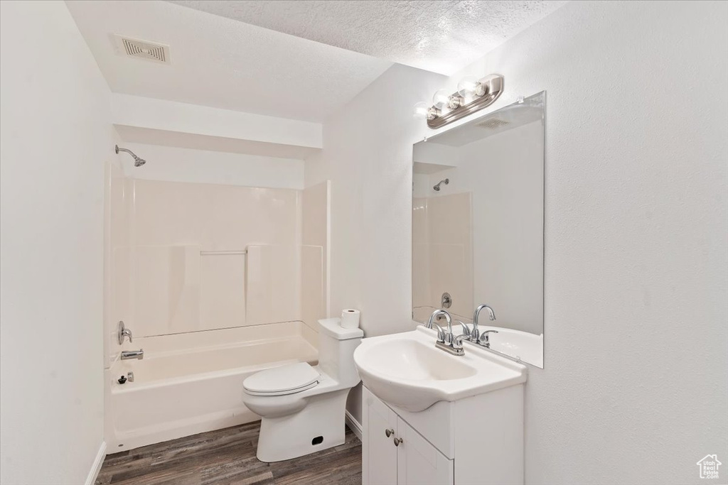 Full bath with wood finished floors, vanity, toilet, shower / bathtub combination, and a textured ceiling
