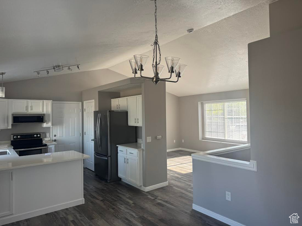 Kitchen featuring appliances with stainless steel finishes, an inviting chandelier, dark wood finished floors, white cabinetry, and vaulted ceiling