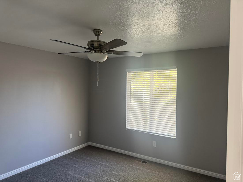 Empty room featuring visible vents, baseboards, dark carpet, ceiling fan, and a textured ceiling