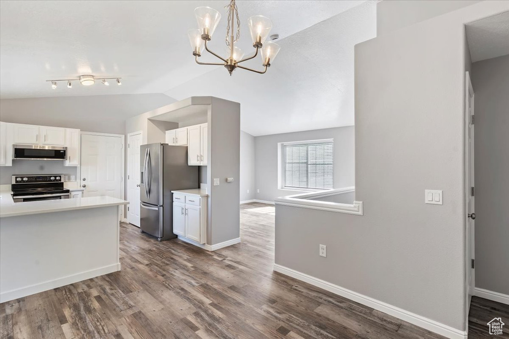 Kitchen featuring stainless steel appliances, vaulted ceiling, white cabinetry, light countertops, and baseboards