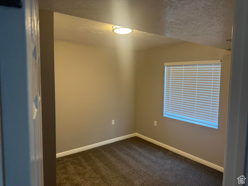 Unfurnished room with baseboards, a textured ceiling, and dark carpet