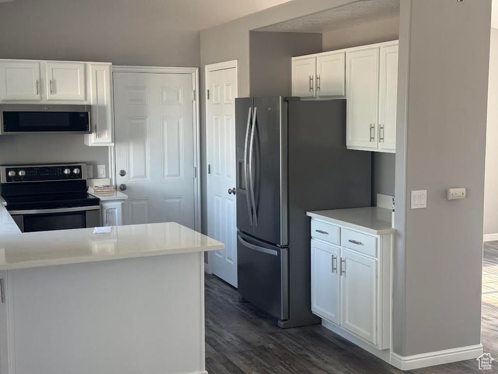Kitchen featuring light countertops, white cabinets, appliances with stainless steel finishes, and dark wood-style floors