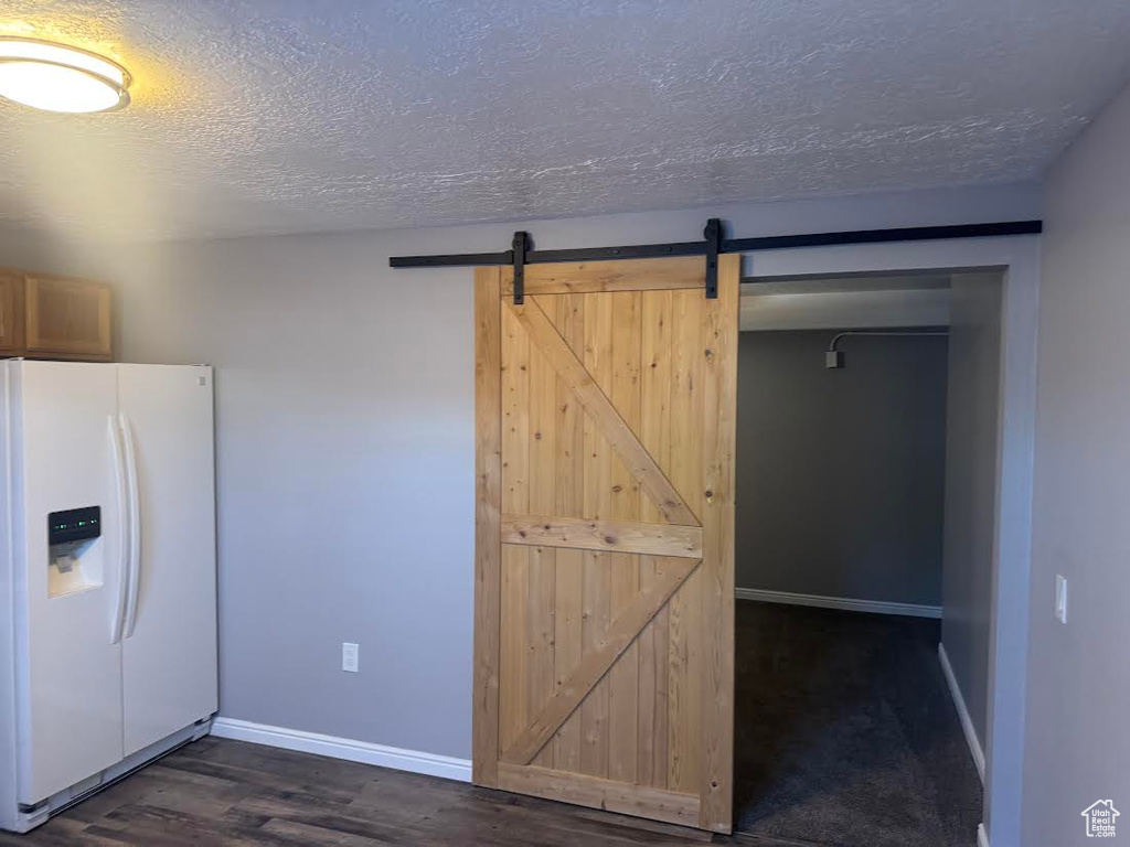 Kitchen with baseboards, a barn door, a textured ceiling, and white refrigerator with ice dispenser