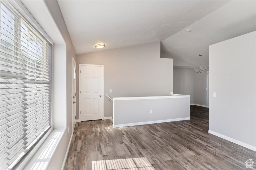 Unfurnished room with vaulted ceiling, a chandelier, wood finished floors, and baseboards