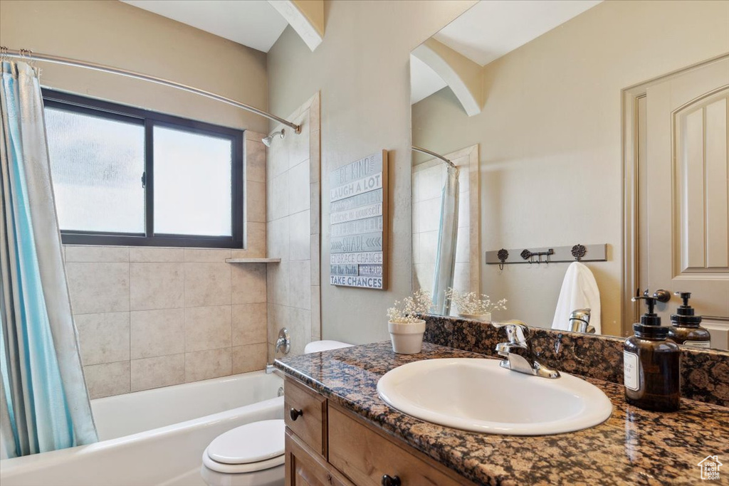 Bathroom featuring vanity, shower / bathtub combination with curtain, and toilet