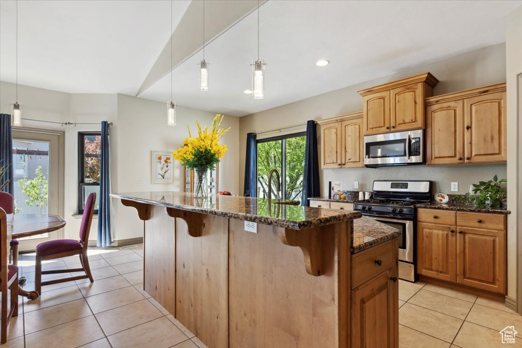 Kitchen featuring appliances with stainless steel finishes, a breakfast bar, dark stone countertops, and light tile patterned flooring