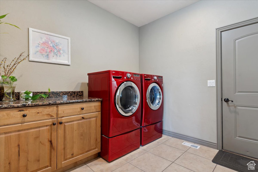 Clothes washing area with separate washer and dryer, cabinet space, light tile patterned floors, and visible vents