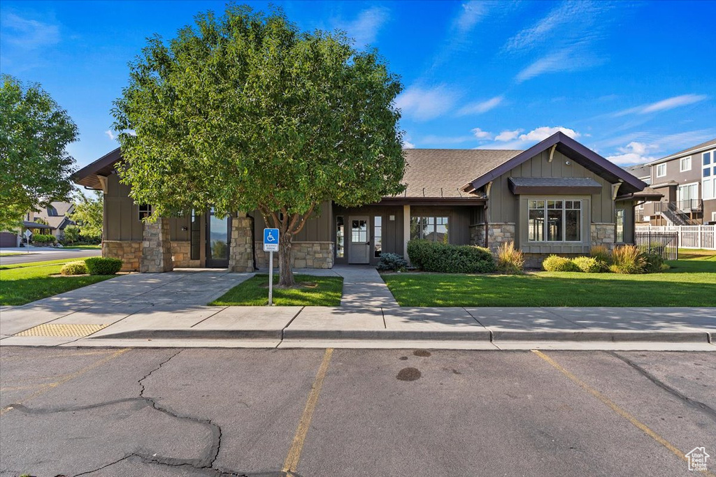 View of front facade with fence, stone siding, board and batten siding, a front yard, and uncovered parking