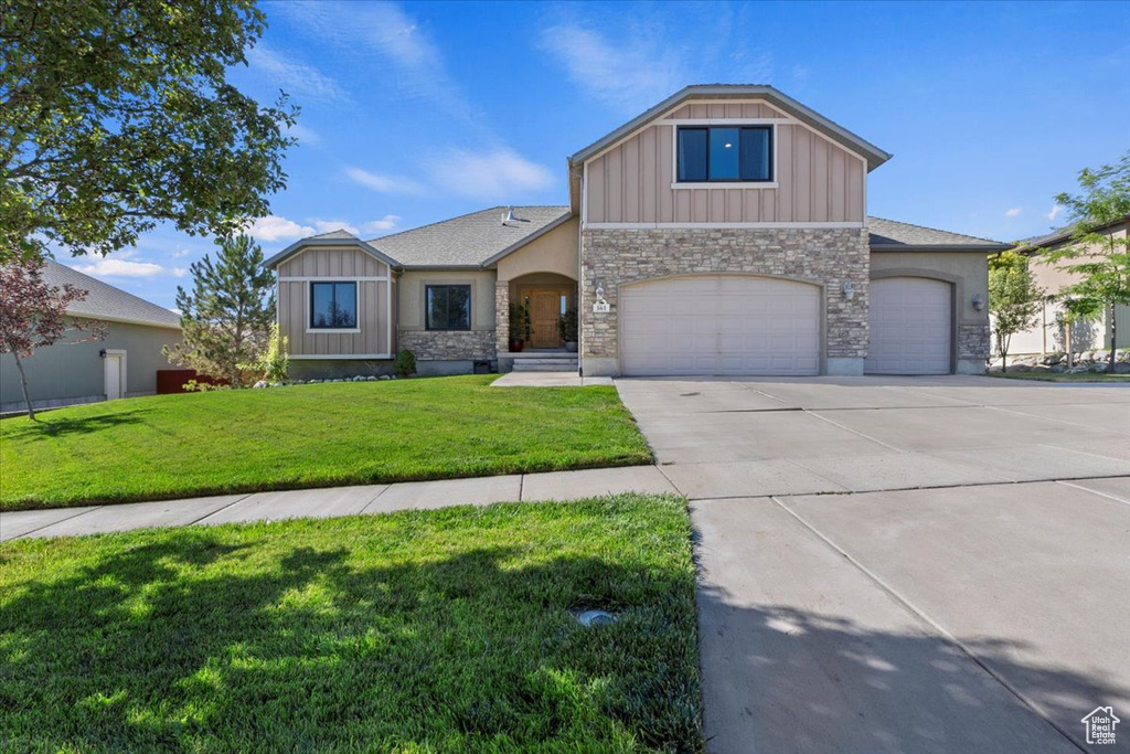 View of front of house with a front lawn, stone siding, board and batten siding, concrete driveway, and an attached garage