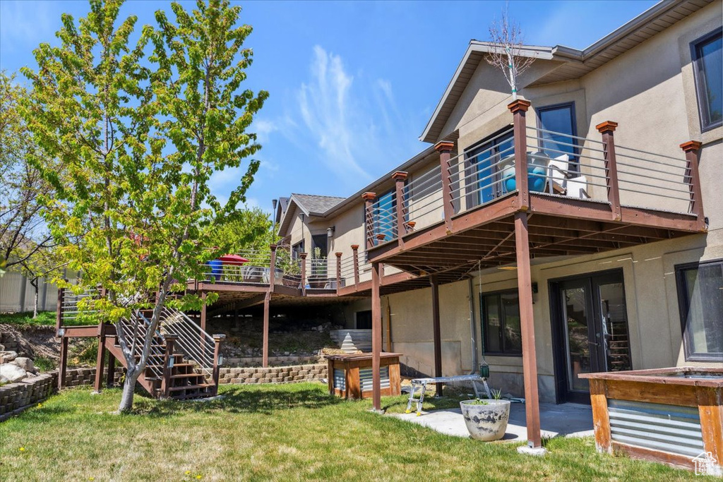 Rear view of house featuring a lawn, a deck, and stucco siding