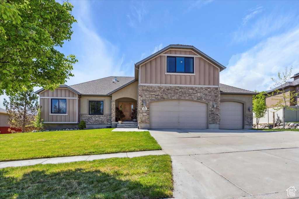 View of front of home with a garage, a front lawn, stone siding, board and batten siding, and driveway