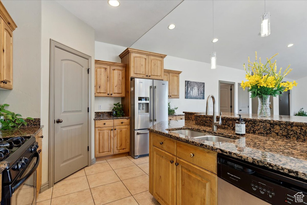 Kitchen featuring dark stone counters, a sink, light tile patterned floors, hanging light fixtures, and stainless steel appliances