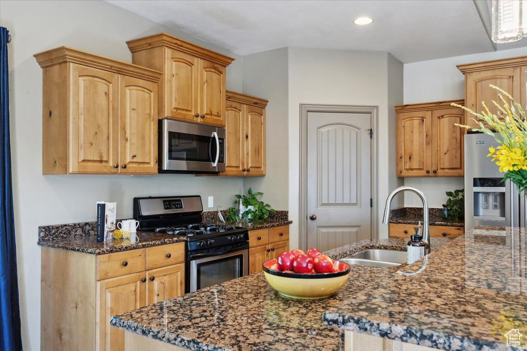 Kitchen featuring appliances with stainless steel finishes, a sink, dark stone countertops, recessed lighting, and an island with sink