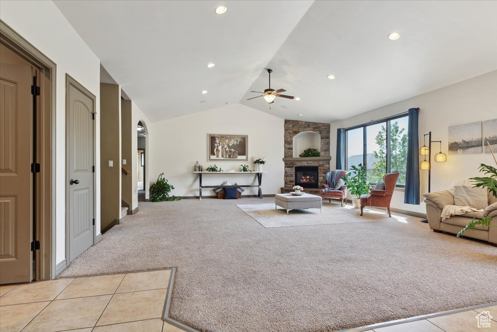 Living area with a fireplace, a ceiling fan, light tile patterned flooring, and light colored carpet