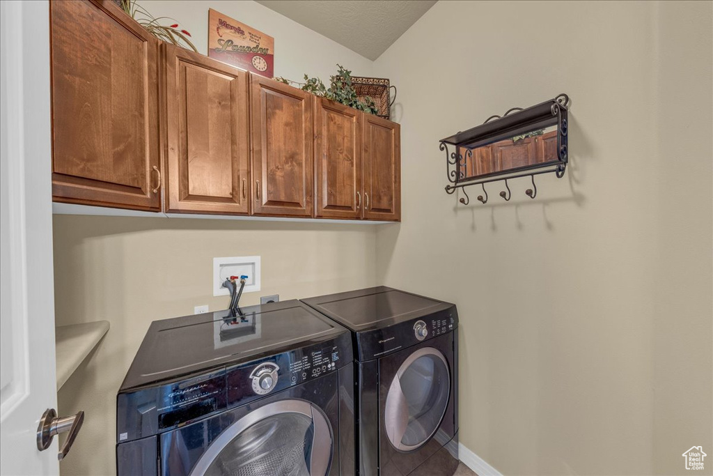 Clothes washing area with tile patterned flooring, cabinet space, baseboards, and washing machine and clothes dryer