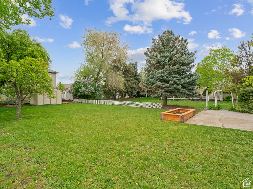 View of yard with a garden, an outbuilding, a patio area, fence, and a storage unit