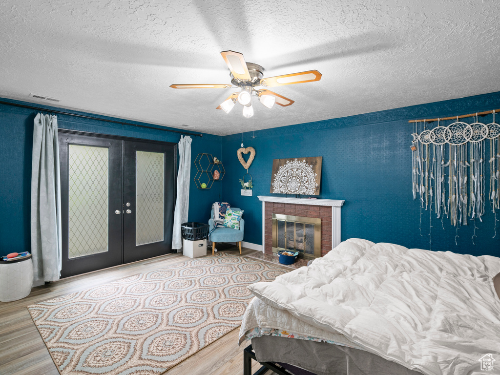 Bedroom featuring ceiling fan, french doors, a textured ceiling, a fireplace with flush hearth, and wood finished floors