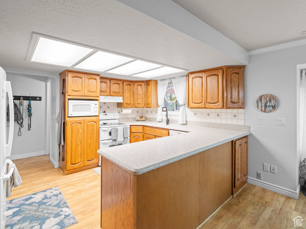Kitchen featuring light wood-style floors, white appliances, light countertops, a peninsula, and decorative backsplash