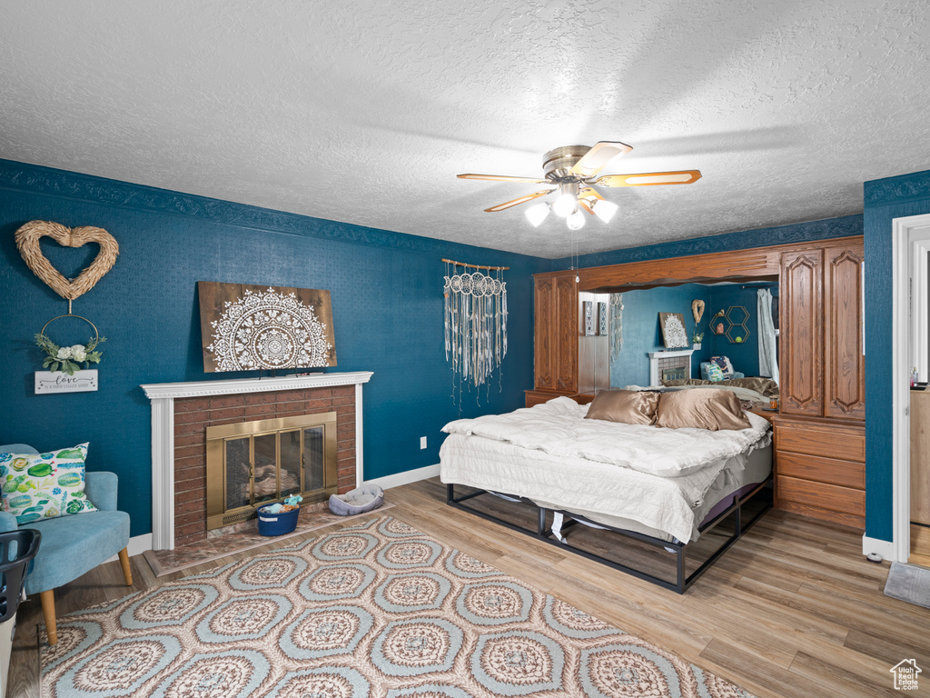 Bedroom featuring wood finished floors, a fireplace, baseboards, a textured ceiling, and a ceiling fan