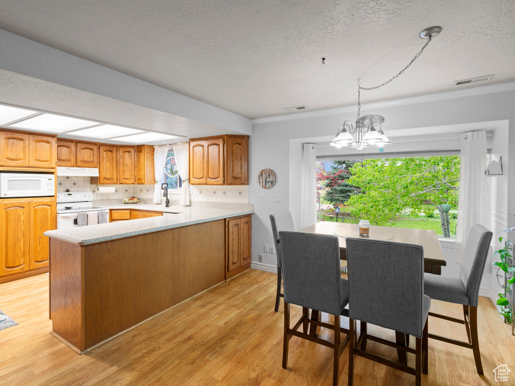 Kitchen featuring white appliances, light countertops, a textured ceiling, under cabinet range hood, and light wood-style flooring