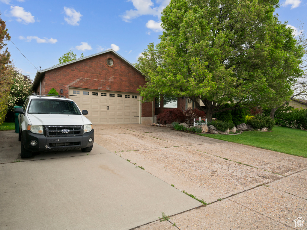 View of front of property featuring concrete driveway, brick siding, an attached garage, and a front yard