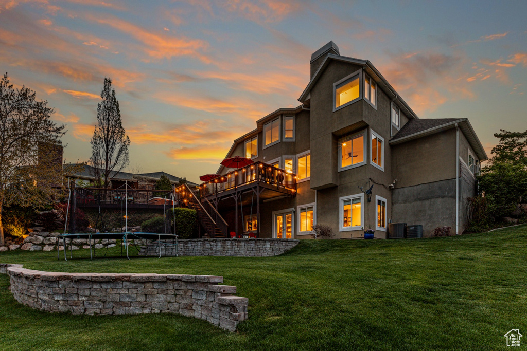 Back of house at dusk with a lawn, a wooden deck, stairs, and a chimney