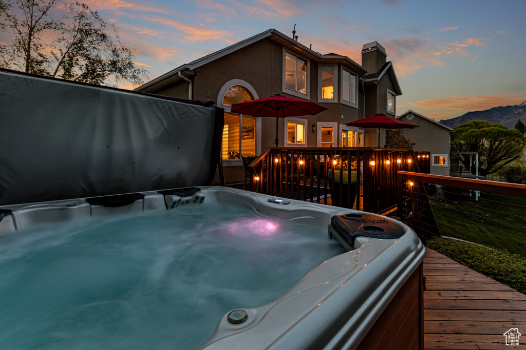 Back of property at dusk with a chimney, a hot tub, stucco siding, and a deck