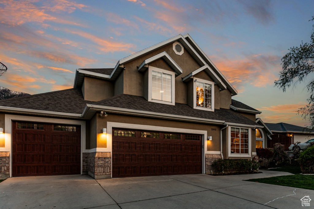 View of front facade with an attached garage, driveway, stone siding, and stucco siding