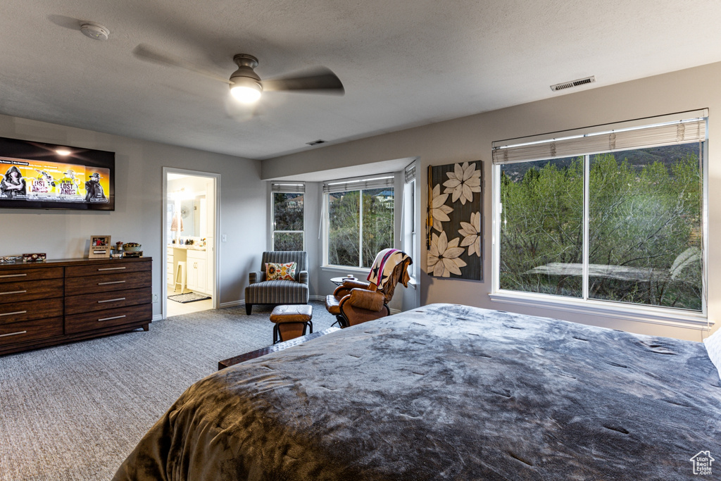 Carpeted bedroom featuring baseboards, ceiling fan, ensuite bath, and visible vents