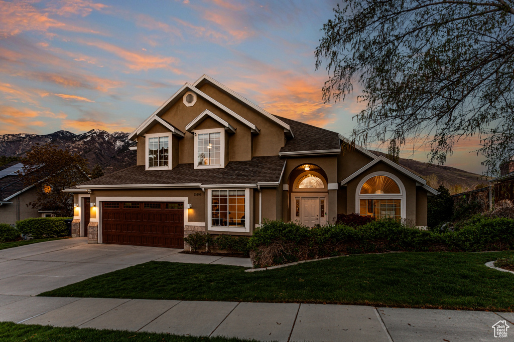 View of front of house featuring driveway, a yard, an attached garage, stone siding, and stucco siding