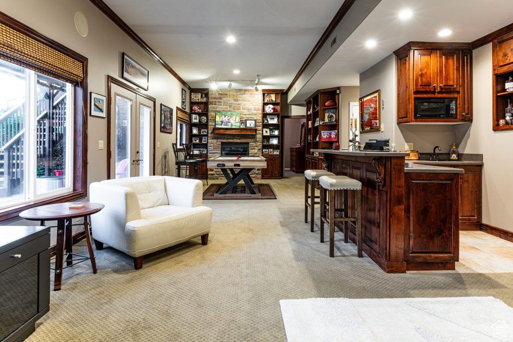 Bar featuring crown molding, light colored carpet, black microwave, a stone fireplace, and indoor wet bar