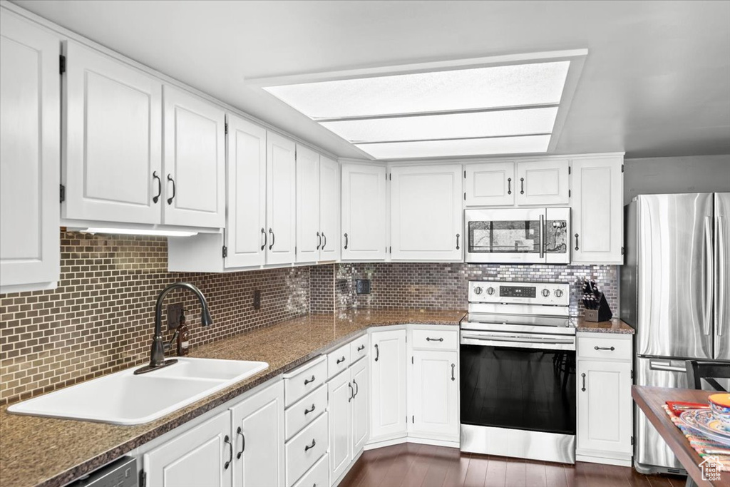 Kitchen with stainless steel appliances, white cabinetry, a sink, and tasteful backsplash