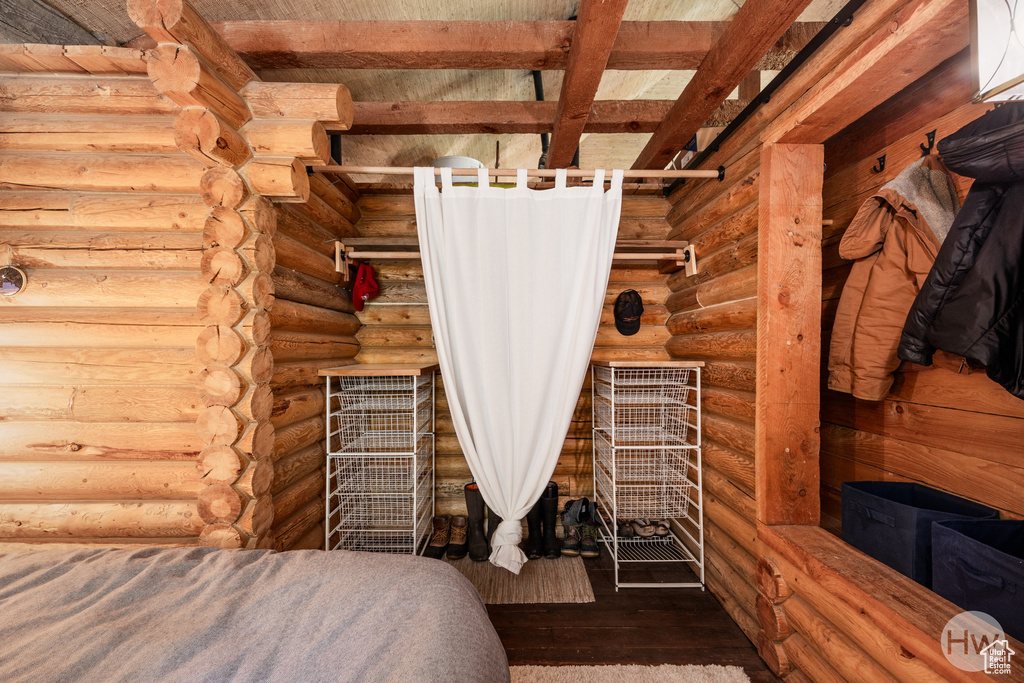 Bedroom featuring beamed ceiling, rustic walls, and wood finished floors