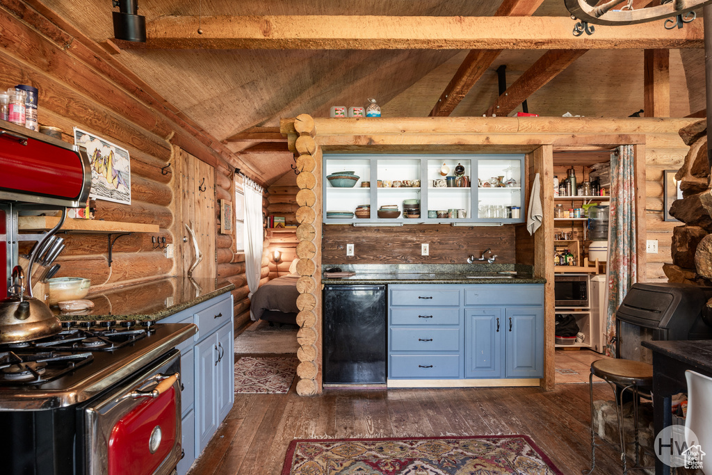 Kitchen with log walls, lofted ceiling with beams, dark wood-style flooring, and appliances with stainless steel finishes