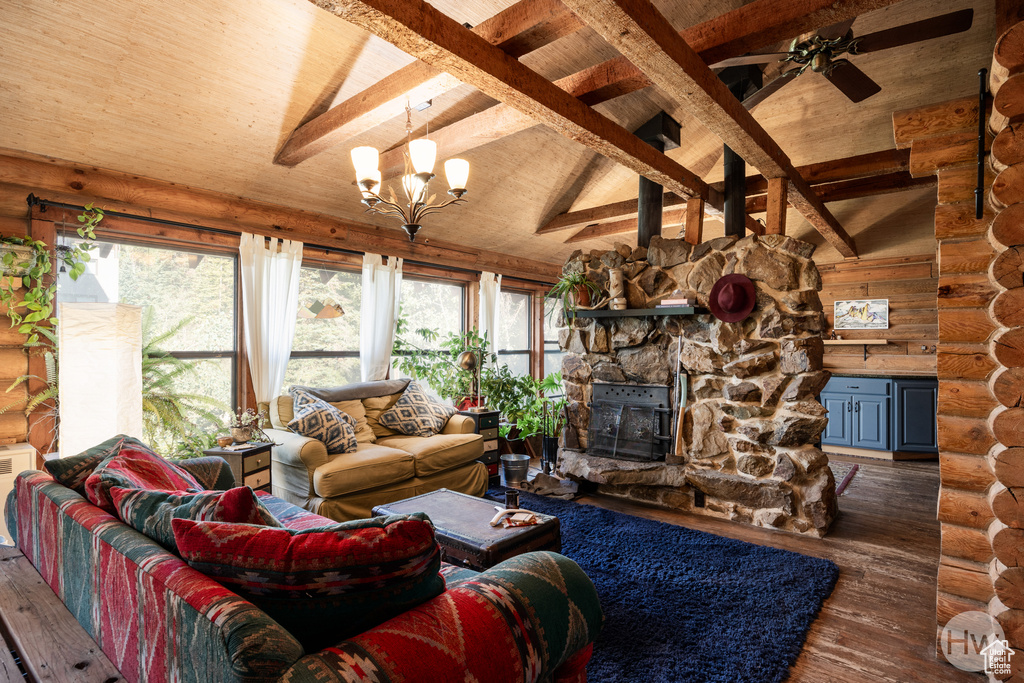 Living room with rustic walls, beam ceiling, a stone fireplace, hardwood / wood-style flooring, and ceiling fan with notable chandelier