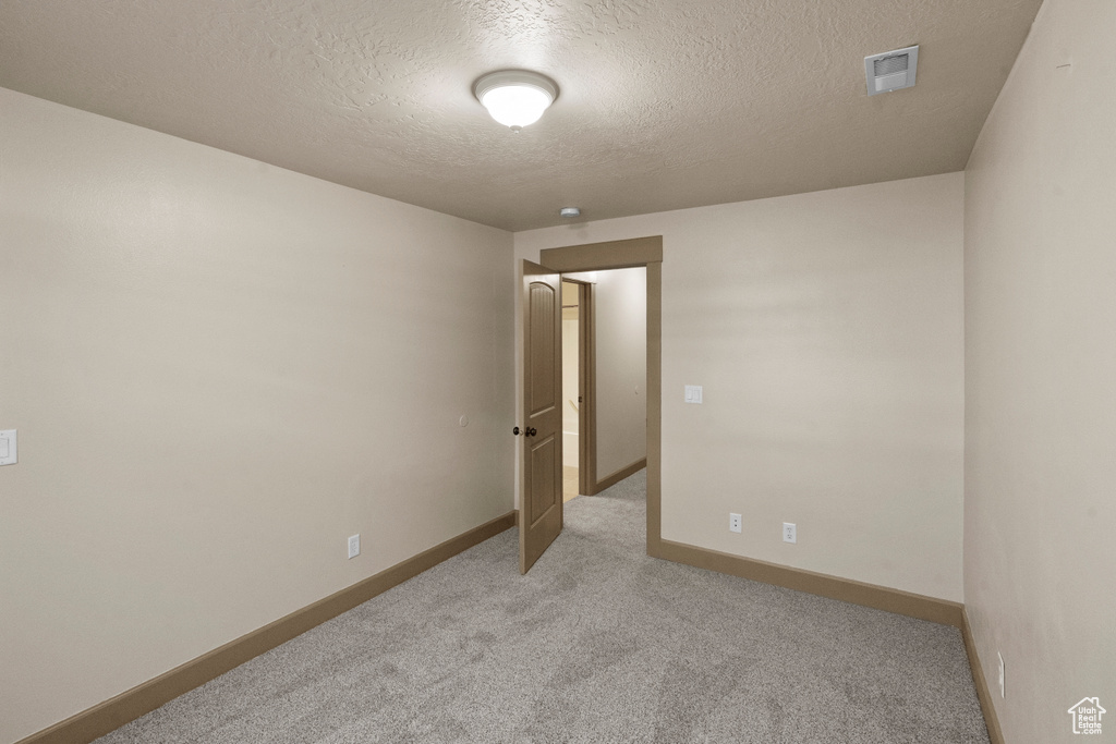 Spare room featuring baseboards, light carpet, a textured ceiling, and visible vents