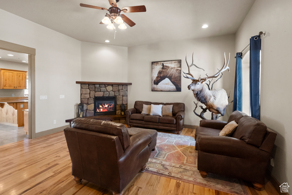 Living room with a stone fireplace, light wood-style flooring, a ceiling fan, baseboards, and recessed lighting