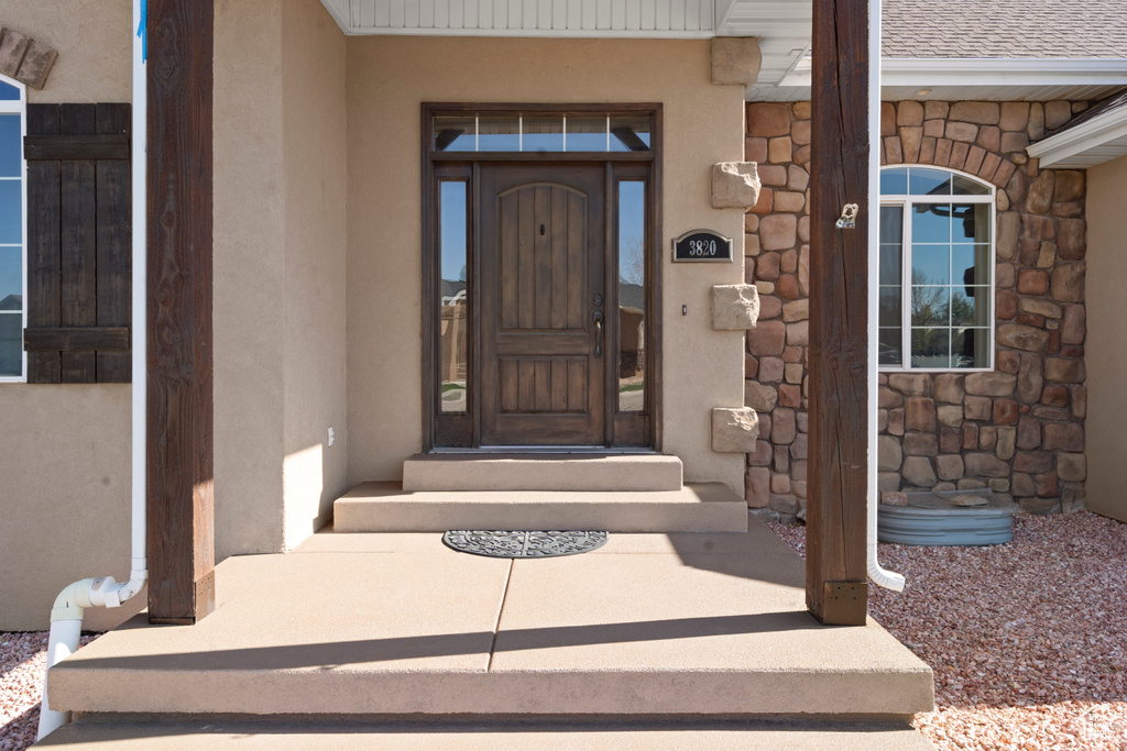 Property entrance with roof with shingles, stone siding, and stucco siding