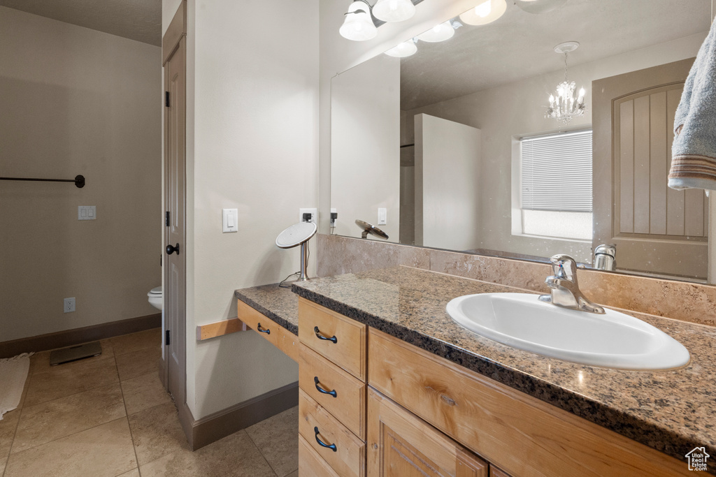 Bathroom featuring an inviting chandelier, vanity, tile patterned flooring, and toilet
