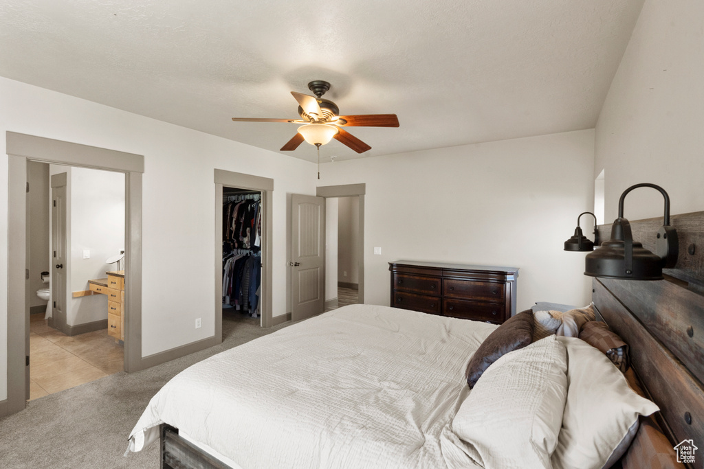 Bedroom with a closet, light carpet, baseboards, ensuite bathroom, and a spacious closet
