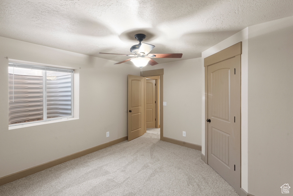 Unfurnished bedroom featuring baseboards, ceiling fan, a textured ceiling, and light colored carpet