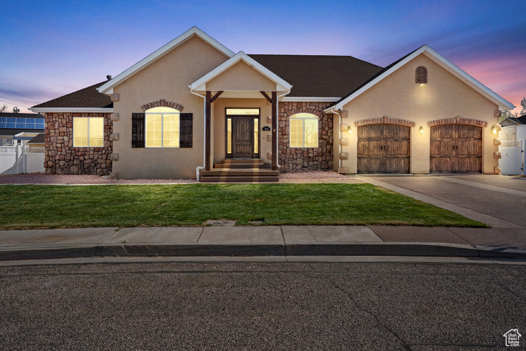 Single story home featuring an attached garage, stone siding, stucco siding, concrete driveway, and a yard