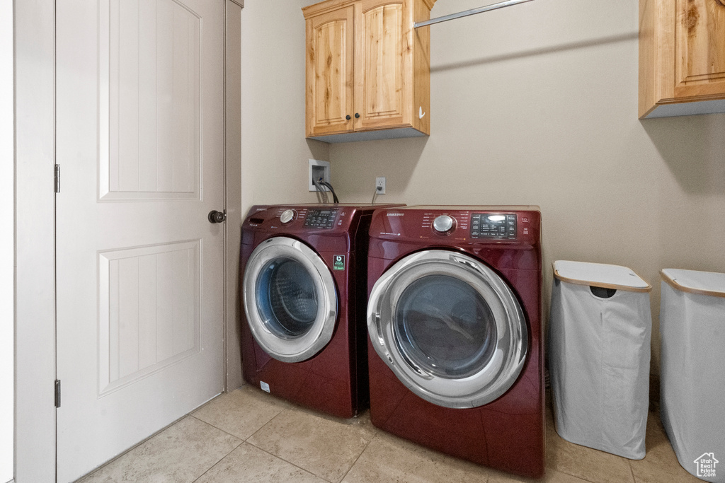 Washroom featuring cabinet space, light tile patterned floors, and washer and dryer