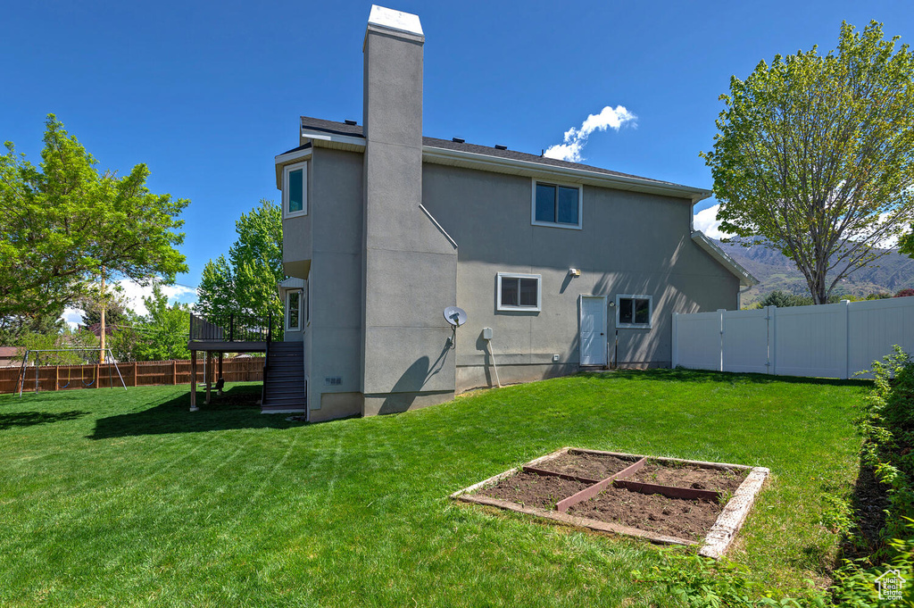 Back of property featuring stucco siding, a vegetable garden, a fenced backyard, a chimney, and a lawn