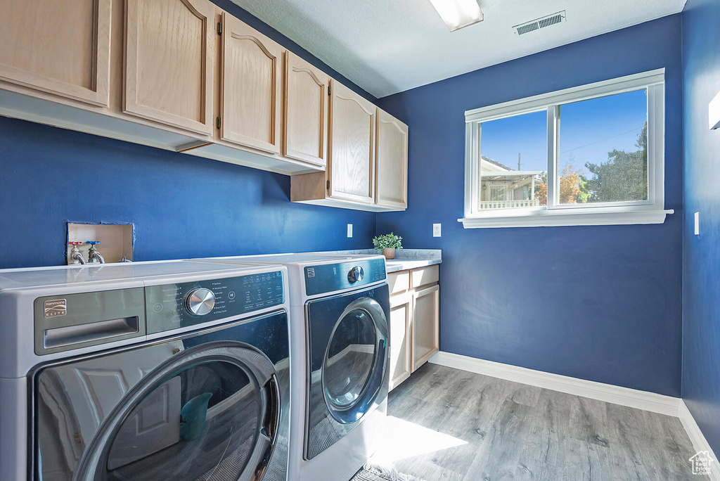 Washroom featuring visible vents, cabinet space, baseboards, light wood-style floors, and washer and dryer