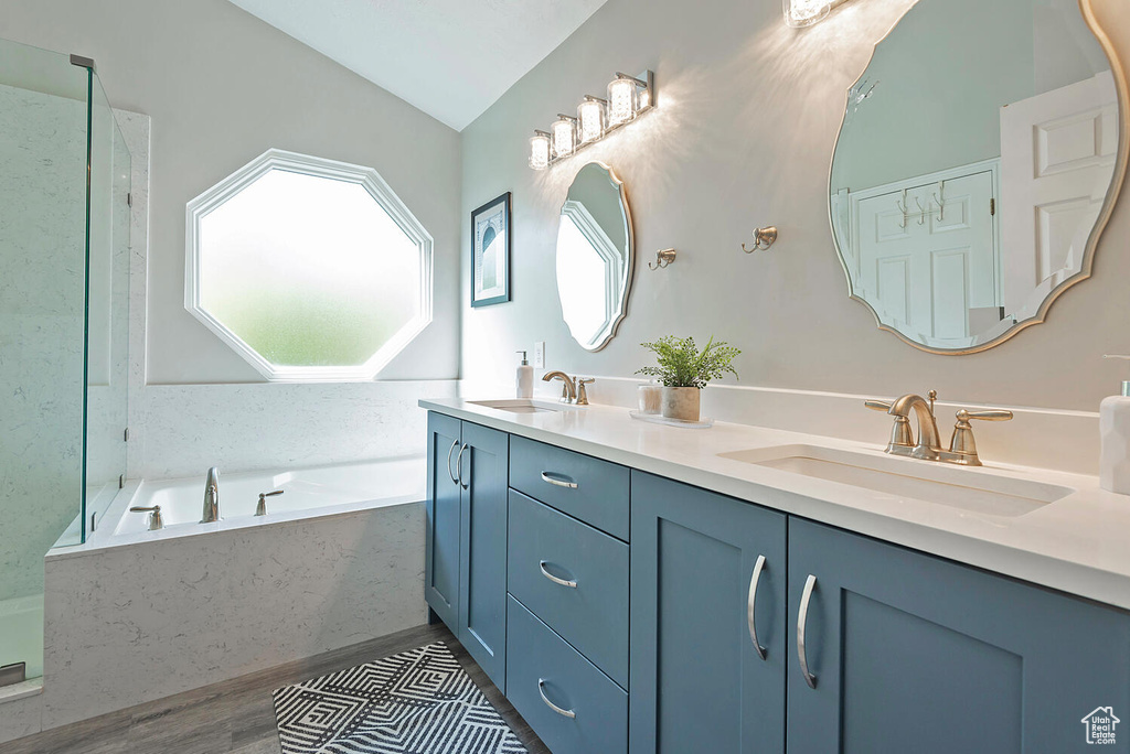 Bathroom featuring a sink, vaulted ceiling, a garden tub, and double vanity