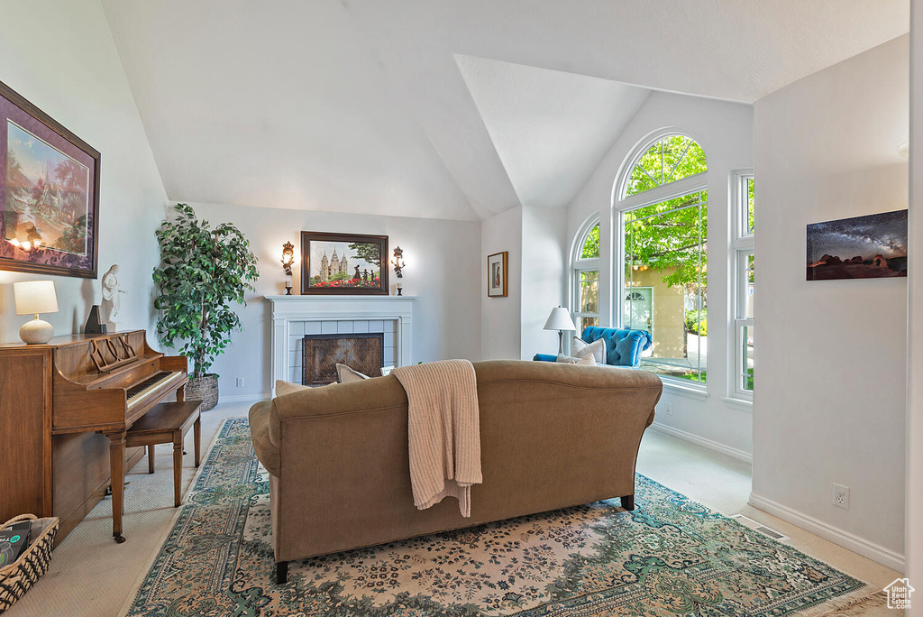 Living area featuring visible vents, a tiled fireplace, light colored carpet, baseboards, and lofted ceiling
