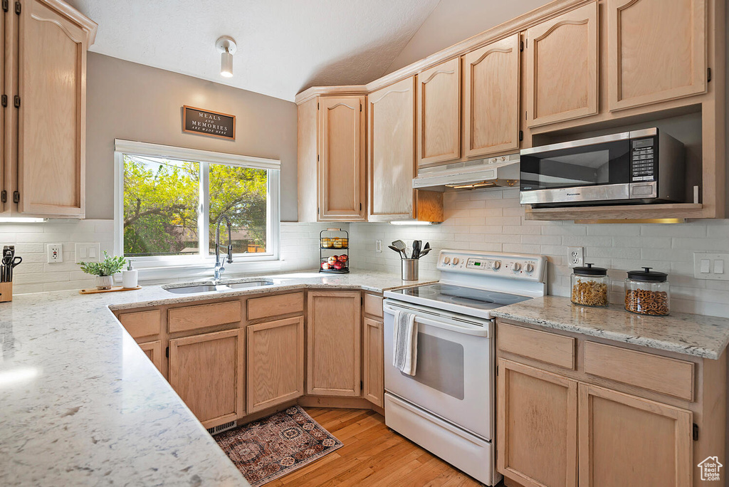 Kitchen with light brown cabinetry, a sink, stainless steel microwave, electric stove, and under cabinet range hood